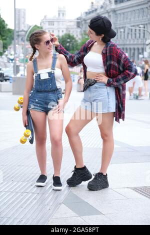 Deux femmes sympa souriant et regardant l'une à l'autre avec un skateboard. Deux amies qui se posent dans la rue. Banque D'Images