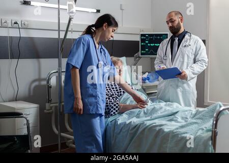 Femme sénior malade recevant des médicaments par voie intraveineuse, se trouvant dans le lit d'hôpital. Mesure par l'infirmière à partir de l'oxymètre fixé sur le doigt du patient. Banque D'Images