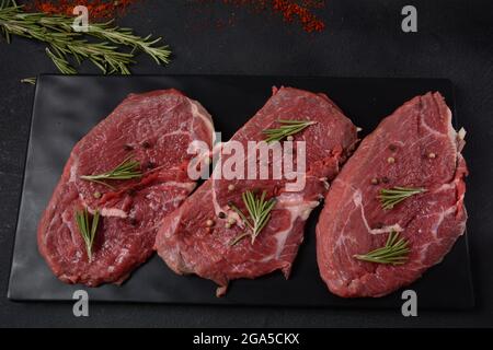 Trois morceaux de bifteck fin traditionnel coupés du filet sur planche à découper en bois avec de l'huile d'olive, du sel, du romarin et du poivre. Black Brut Angus Prim Banque D'Images