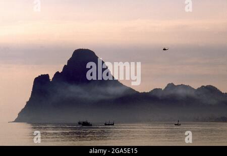 Thaïlande: Bateaux de pêche tôt le matin sur Ao Prachuap (baie de Prachuap), Prachuap Khiri Khan. En termes historiques, Prachuap est l'un des sept points d'atterrissage où les troupes impériales japonaises ont pris d'assaut à terre en 1941, sur leur chemin vers le sud pour occuper Malaya et Singapour. La ville est entourée par des montagnes de calcaire accidentées, dont Khao Chong Krajok, ou « montagne du tunnel miroir », est percée d’une ouverture naturelle qui ne ressemble pas à un miroir géant, et qui est peut-être le plus célèbre monument naturel de la ville. Banque D'Images