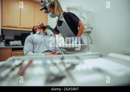 Une infirmière caucasienne vérifie le canal racine des clients mâles avant une opération majeure. Assis dans une chaise de dentiste Banque D'Images