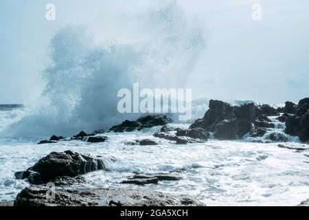 Une puissante vague océanique éclabousse sur un grand rocher au milieu de la mer agitée. Banque D'Images