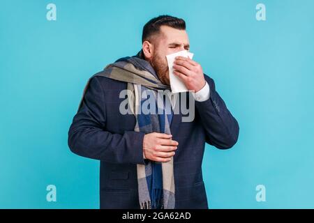 Rhume et grippe. Portrait d'un jeune homme d'affaires barbu malade en costume élégant debout, tenant le tissu sur la bouche et le nez, enveloppé dans une écharpe chaude. Indo Banque D'Images