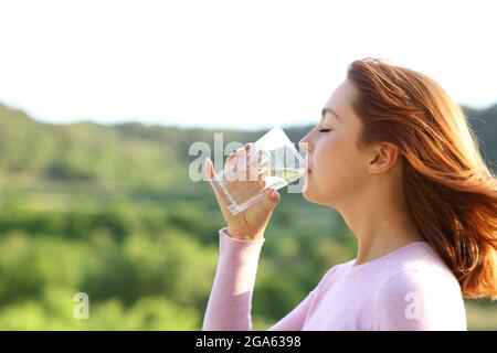 Profil d'une femme buvant de l'eau du verre en plein air dans la nature Banque D'Images