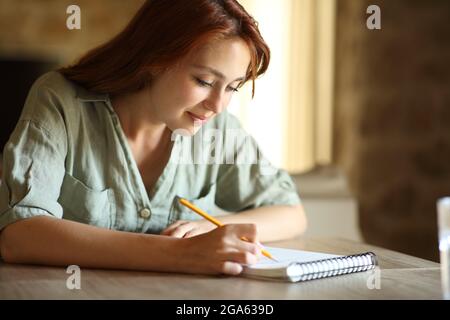 Femme qui dessine ou prend des notes sur un bloc-notes en papier sur une table à la maison Banque D'Images