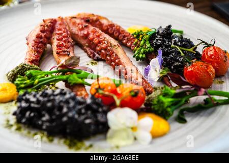 Poulpe avec risotto noir. Crème de carottes, mini-brocoli, pesto de basilic. Une délicieuse cuisine traditionnelle saine est servie pour le déjeuner dans une cuisine gastronomique moderne Banque D'Images