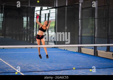 Femme jouant de padel dans un terrain de padel d'herbe bleue intérieur - jeune femme sportive joueur de padel frappant le ballon avec une raquette Banque D'Images