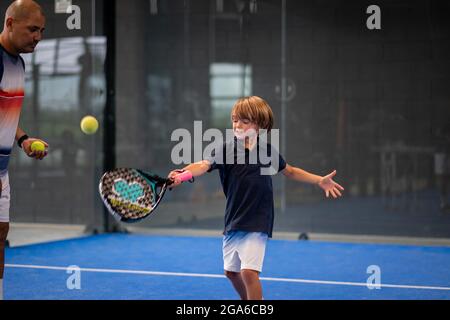 Surveiller l'enseignement de la classe de padel à l'enfant, son étudiant - formateur enseigne à petit garçon comment jouer de padel sur un court de tennis intérieur Banque D'Images