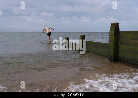 Un nageur sauvage plonge au large d'une groyne de défense de la mer sur la plage dans les eaux de marée froide de l'estuaire de la Tamise, le 25 juillet 2021, à Whitstable, en Angleterre. Banque D'Images