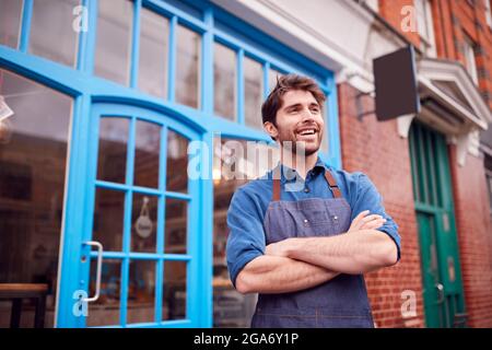 Un homme souriant, propriétaire d'une petite entreprise, portant un tablier devant le magasin de la rue locale High Street Banque D'Images