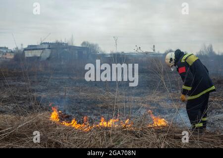 Un pompier éteint l'herbe sèche. Un pompier lutte contre un incendie dans une zone ouverte. Mesures de secours contre les flammes. Une catastrophe écologique brûlée Banque D'Images