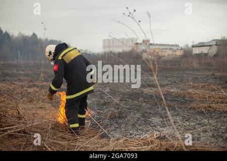 Un pompier éteint l'herbe sèche. Un pompier lutte contre un incendie dans une zone ouverte. Mesures de secours contre les flammes. Une catastrophe écologique brûlée Banque D'Images