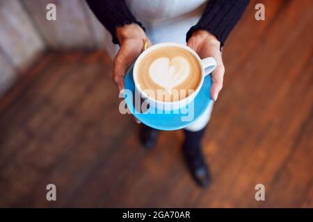 Gros plan de la serveuse au café-restaurant tenant une tasse avec coeur Design versé dans le lait Banque D'Images