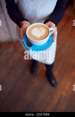Gros plan de la serveuse au café-restaurant tenant une tasse avec coeur Design versé dans le lait Banque D'Images