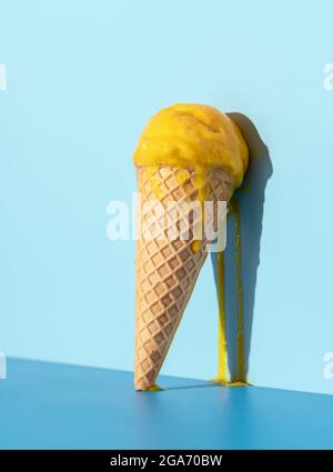 Glace fondue à la mangue qui coule sur un mur bleu. Crème glacée à la mangue dans un cône de gaufres en lumière vive Banque D'Images