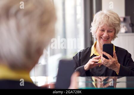 Femme senior attendant d'avoir la coupe de cheveux dans salon de coiffure regardant le téléphone mobile Banque D'Images