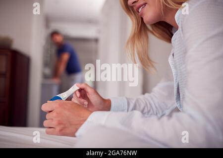 Gros plan de femme souriante portant un pyjama dans la chambre tenant le test de grossesse positif Banque D'Images