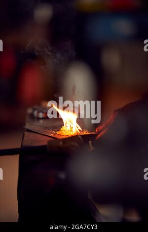 Gros plan de Male Blacksmith éclairage des sculptures en bois sur l'enclume pour commencer le feu dans Forge Banque D'Images