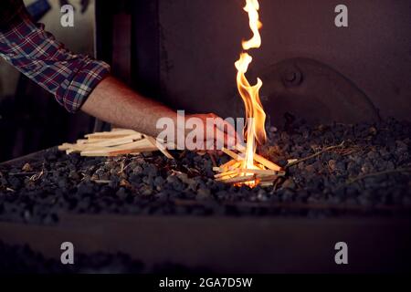 Gros plan de Male Blacksmith Lighting Bois pour commencer Blaze dans Forge Banque D'Images