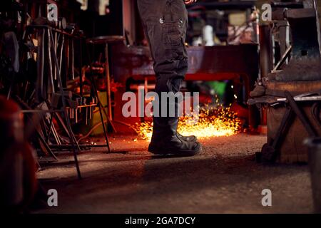 Gros plan de Male Blacksmith debout à côté d'Anvil entouré de Sparks et d'Embers Banque D'Images