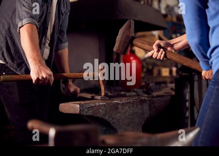 Gros plan de deux Blacksmiths martelant Metalwork sur Anvil Banque D'Images