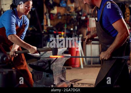 Les Blacksmiths mâles et femelles martètent des métaux sur Anvil avec des Sparks Banque D'Images