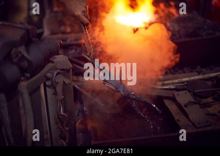 Gros plan de Male Blacksmith Cooling Metalwork dans l'eau après avoir sorti de Forge Banque D'Images