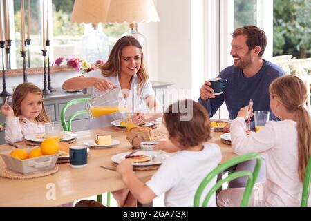 Famille portant un pyjama assis autour de la table en dégustant un petit déjeuner à crêpes ensemble Banque D'Images