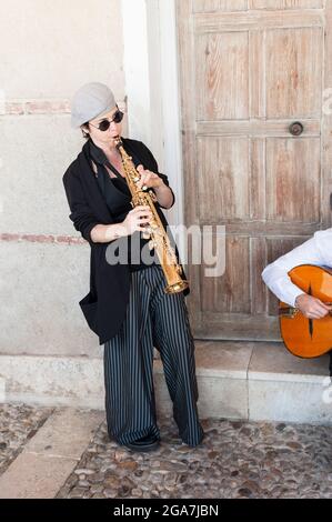 Musiciens de jazz vêtus de style rétro jouant dans la rue. Une femme brune debout avec chapeau et lunettes de soleil jouant clarinette au premier plan et Banque D'Images