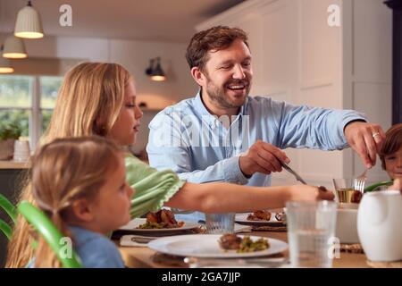Famille assis autour de la table à la maison en appréciant le repas ensemble Banque D'Images