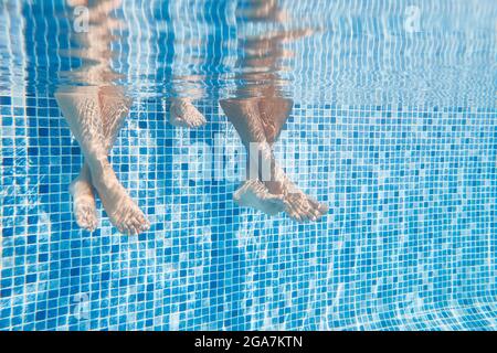 Photo sous-marine des jambes de couples comme ils s'assoient sur le bord de la piscine en vacances Banque D'Images