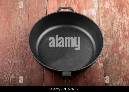 Poêle noire sans poignée sur fond en bois rouge. Banque D'Images