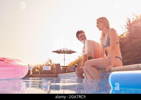 Couple aimant pendant les vacances d'été assis au bord de la piscine Banque D'Images