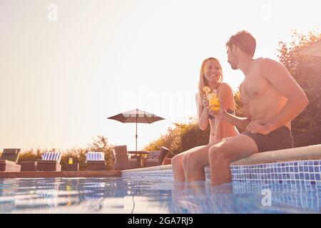 Couple aimant pendant les vacances d'été assis au bord de la piscine avec des boissons froides Banque D'Images