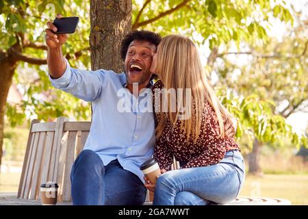 Couple d'âge mûr posant pour Selfie sur téléphone portable assis sur le siège dans le parc Banque D'Images