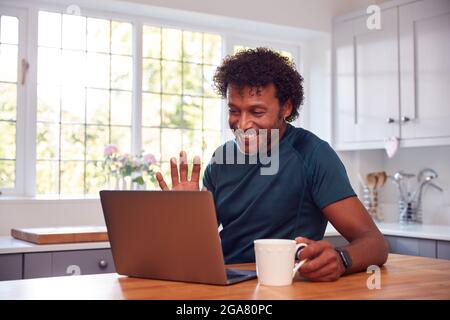 Homme mature à la maison dans la cuisine agitant comme il fait appel vidéo sur ordinateur portable Banque D'Images