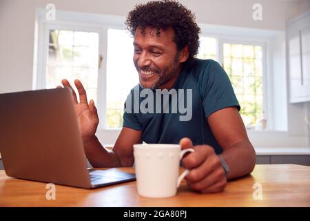 Homme mature à la maison dans la cuisine agitant comme il fait appel vidéo sur ordinateur portable Banque D'Images