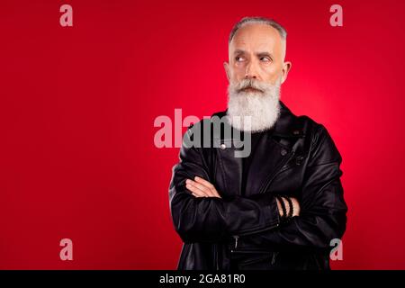 Photo de sérieux confiant vieux homme look vide espace croix mains porter une veste en cuir isolée sur fond rouge couleur Banque D'Images