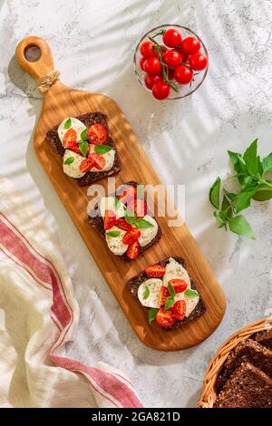 Sandwichs au pain de blé entier avec fromage, tomates et feuilles de basilic, vue de dessus. Concept d'en-cas sain. Banque D'Images
