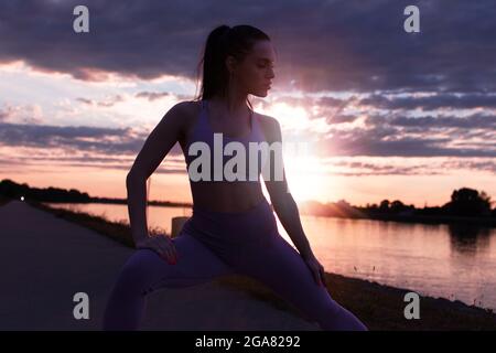 Jeune femme en vêtements de sport s'étirant avant de courir au lever du soleil, réchauffez-vous Banque D'Images