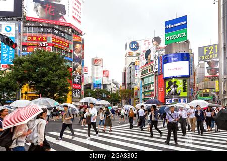 Tokyo, Japon - 21 juin 2016 : les rues animées de Tokyo par un jour de pluie. De nombreuses personnes portant des parasols traversent l'intersection très fréquentée de Shibuya Crossing. Banque D'Images