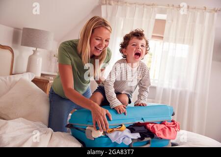 Mère et fils emballage pour les vacances avec le garçon debout sur la pleine Suitcase à fermer Banque D'Images