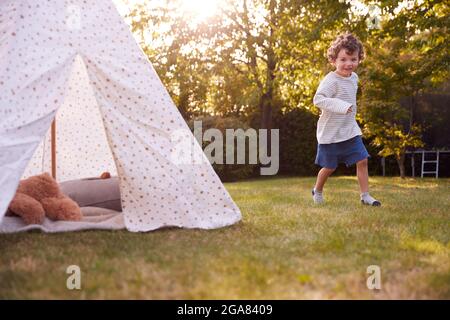 Jeune garçon courant et s'amuser avec une tente ou un tipi perché dans le jardin Banque D'Images