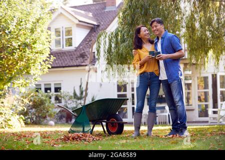 Couple asiatique mature prenant UNE pause avec des boissons chaudes tout en laquant le jardin avec le Rake et le Barrow Banque D'Images