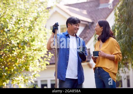 Couple asiatique mature prenant UNE pause avec des boissons chaudes tout en laquant jardin avec Rake Banque D'Images
