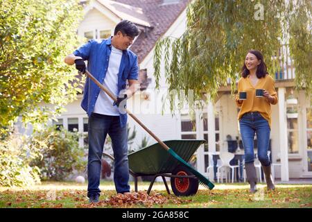 Femme asiatique mature apportant une boisson chaude au jardin de l'homme fatiguant avec le Rake Banque D'Images