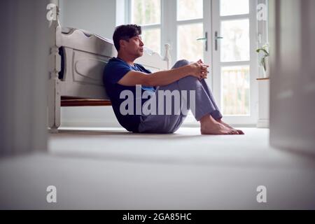 Malheureux et déprimé homme asiatique mûr dans un pyjama assis à l'étage de la chambre Banque D'Images