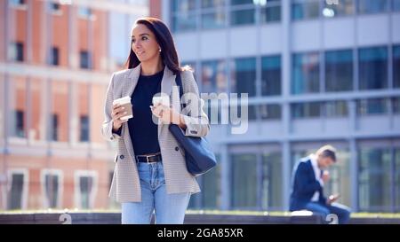 Femme d'affaires avec café Takeaway à pied au bureau tenant le téléphone mobile Banque D'Images