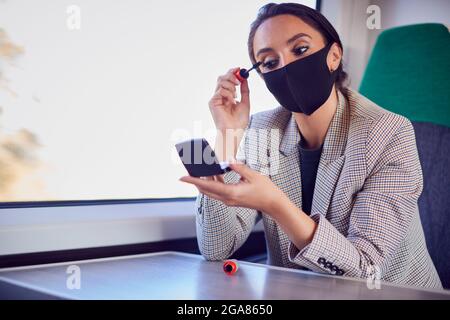 Femme d'affaires en train de mettre sur le maquillage tout en portant un masque facial d'EPI pendant la pandémie de santé Banque D'Images