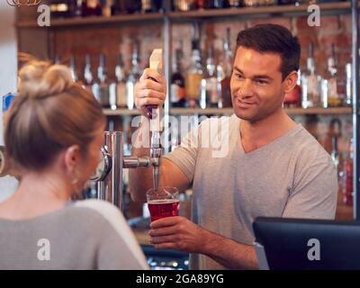 Barman souriant derrière le comptoir servant une cliente féminine avec de la bière Banque D'Images